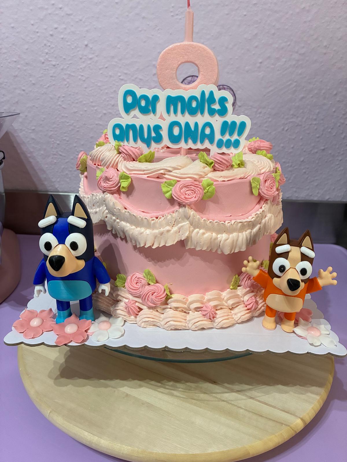Tarta de cumpleaños de Lali.reposteria con topper 'Per molts anys ONA!!!' y figuras de Bluey impresas en 3D